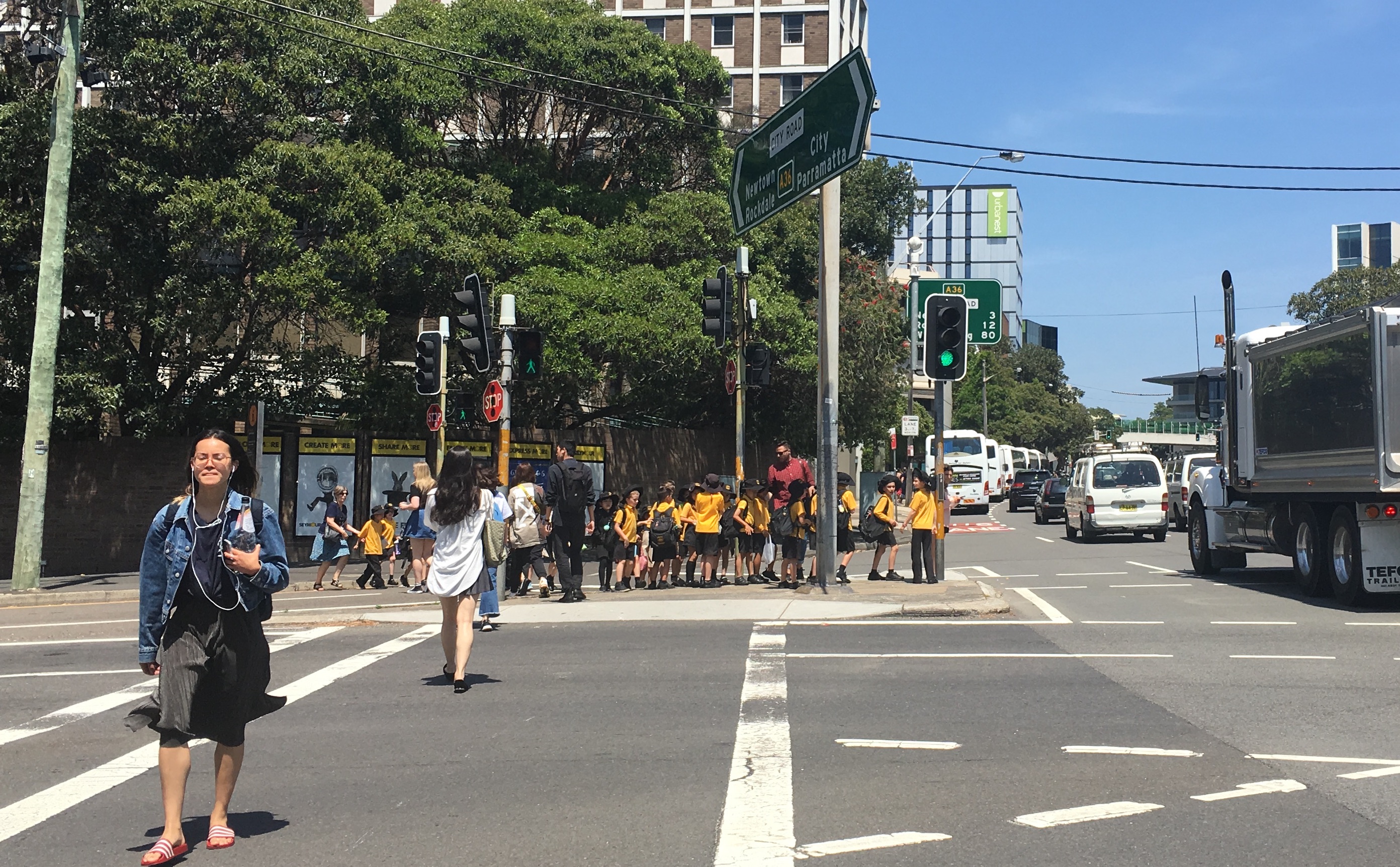 At least 20 people, most of them children, queued up like bowling pins, on a refugee island at City Road and Cleveland Street, Sydney. Other groups are held back at the Seymour Centre, or have been already ferried across City Road to Victoria Park. This is typical, but not good, urban design.